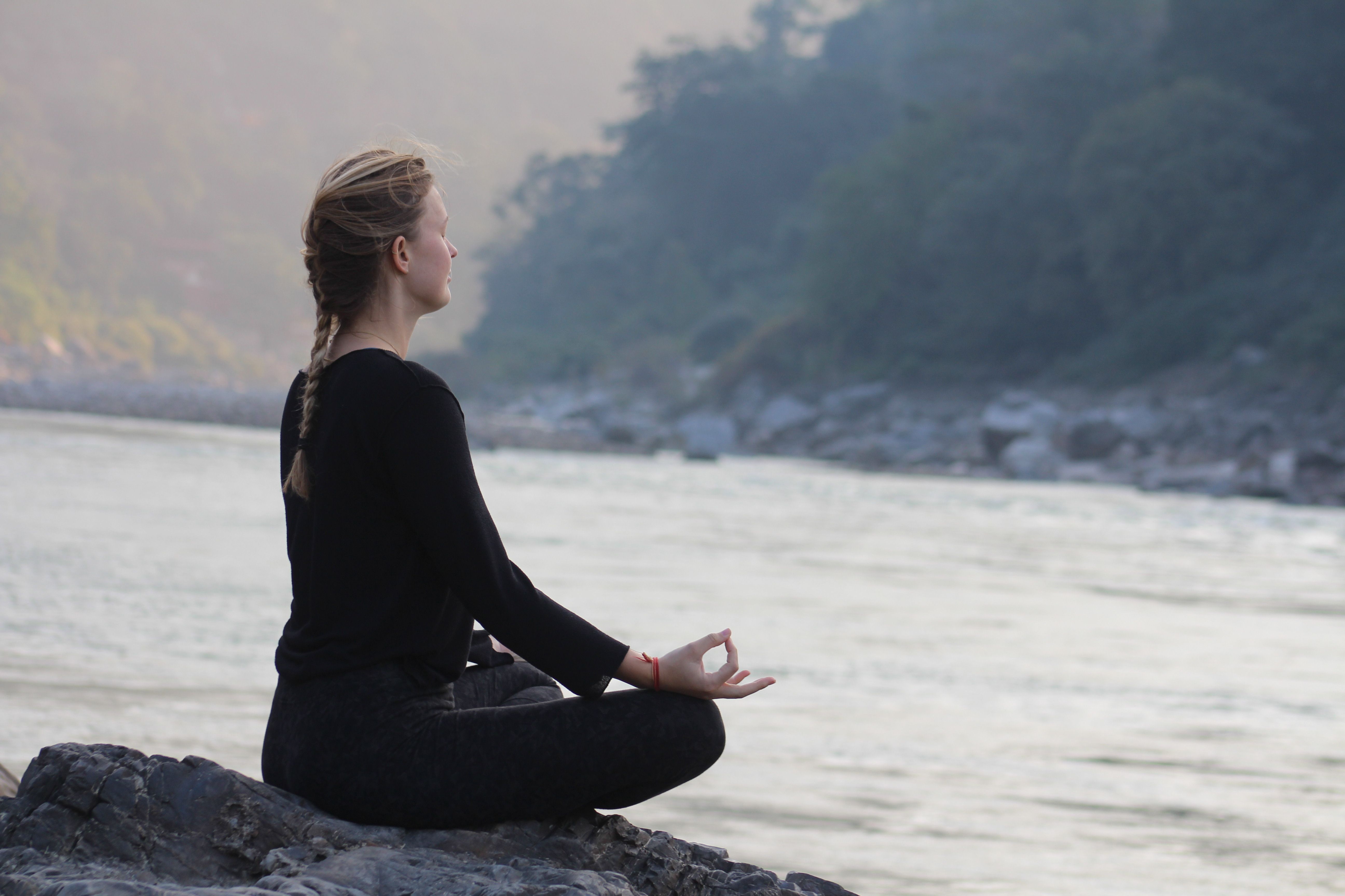 Person meditating by a river at dawn